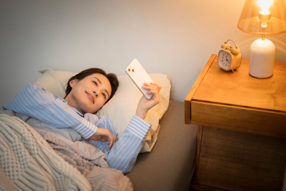 夜、ベッドでスマートフォンの動画を眺める女性